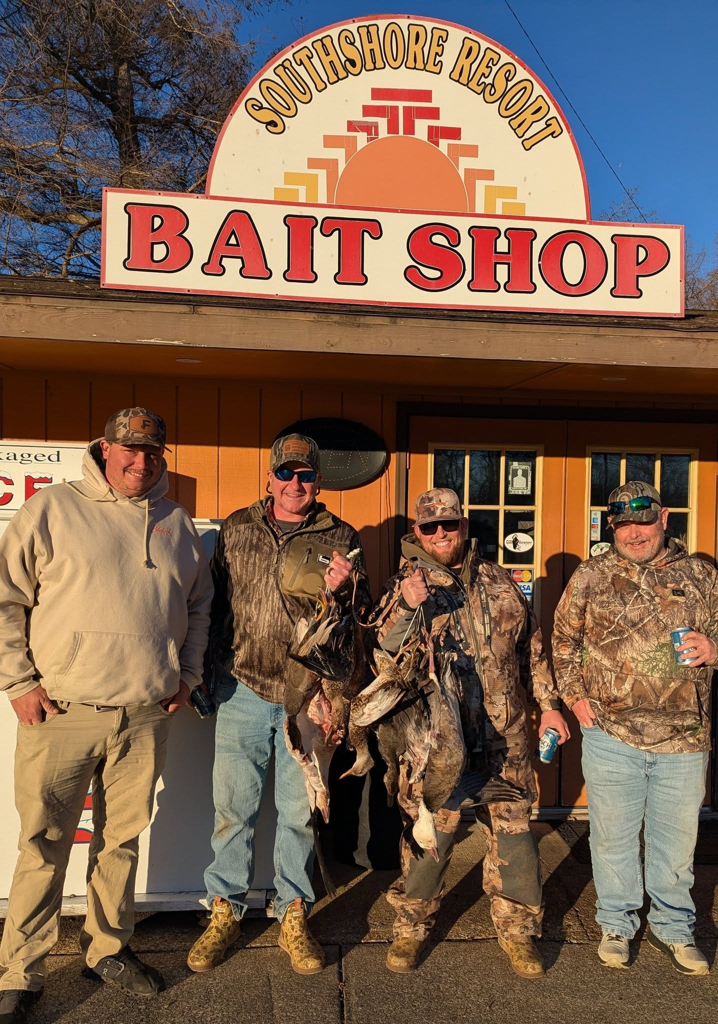 Hunters with duck catch in front of the Bait Shop sign