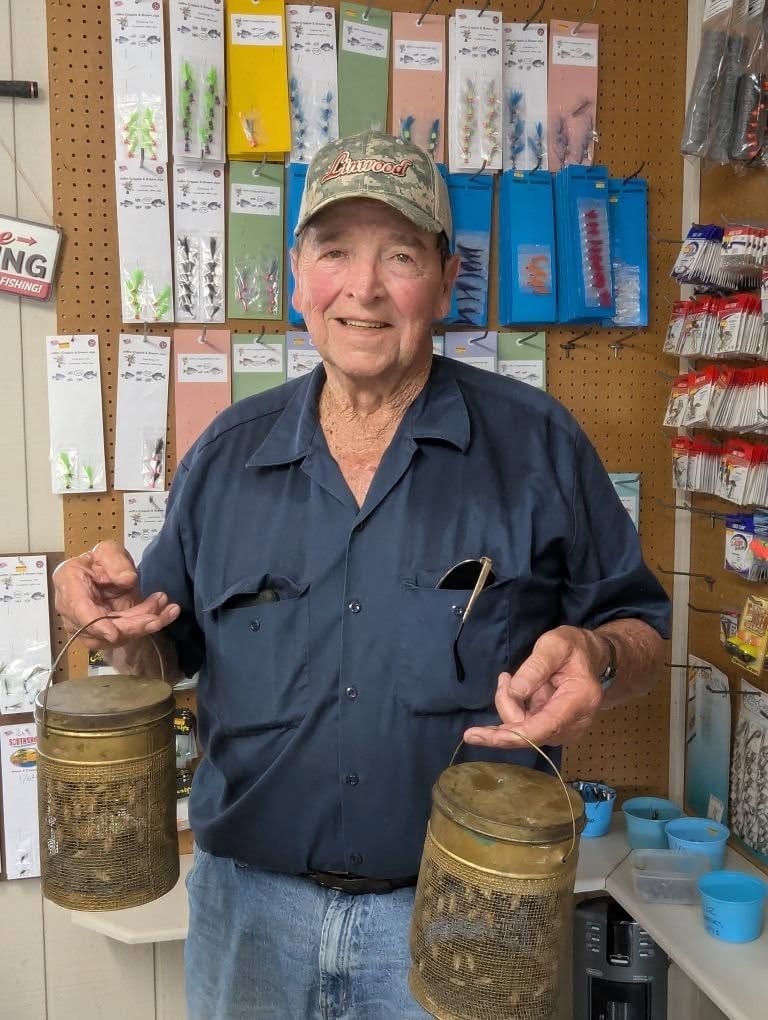Linwood holding antique mesh bait buckets in front of the tackle wall