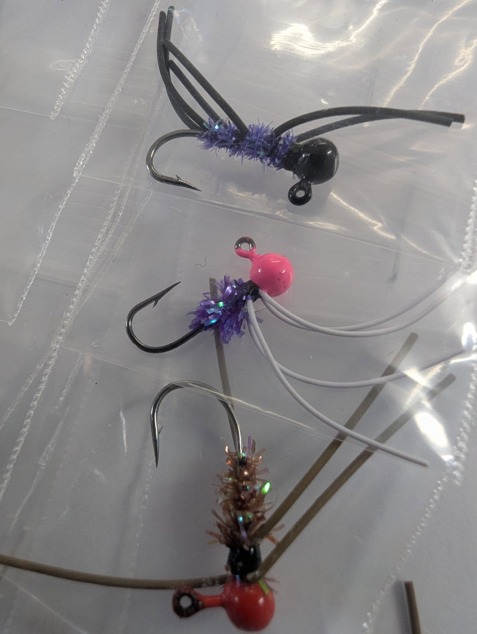 Three hand-tied crappie jigs — black, pink, and copper — in a clear bag