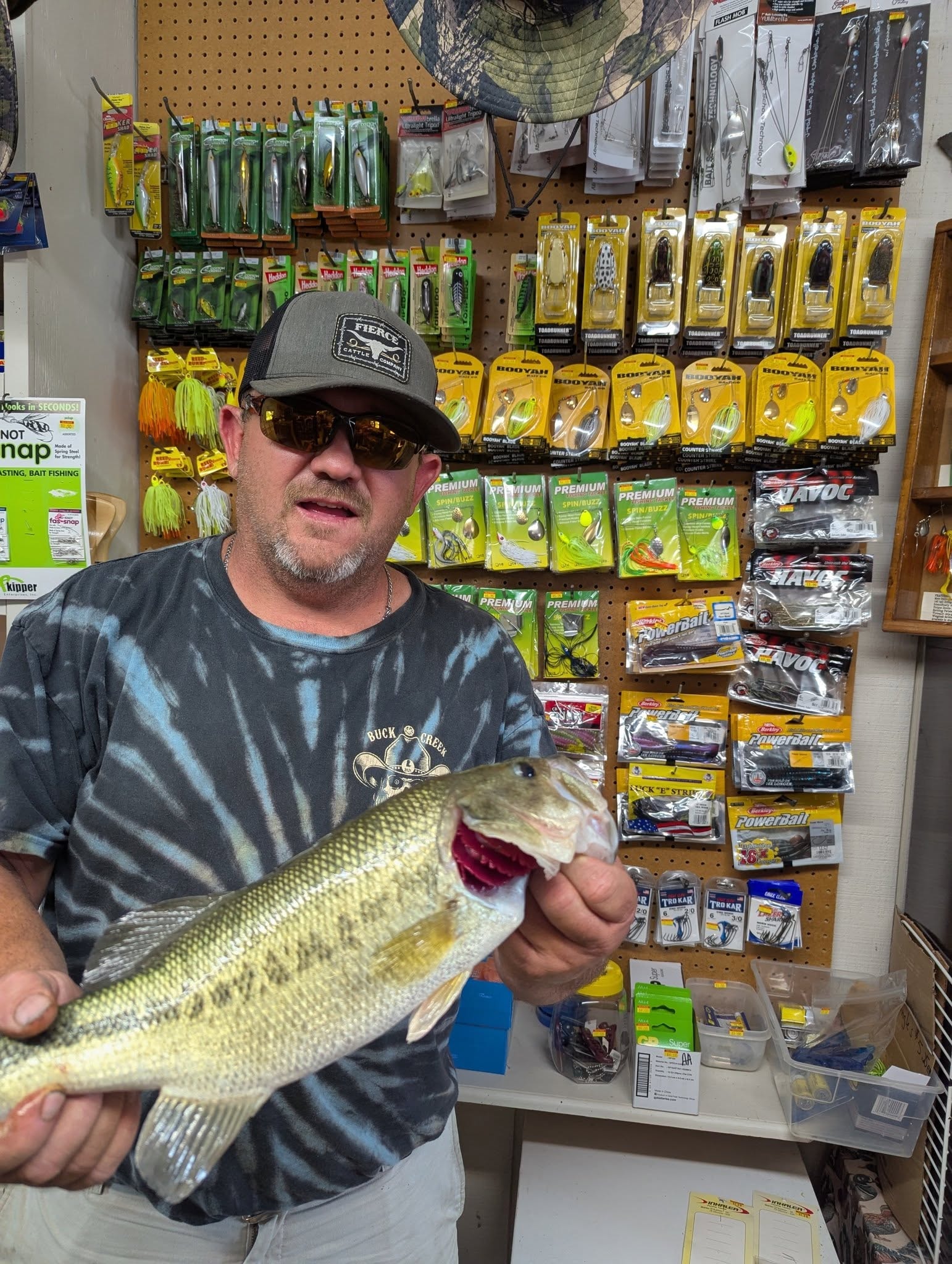 Man holding a large bass in front of the Booyah and Premium Tackle pegboard wall