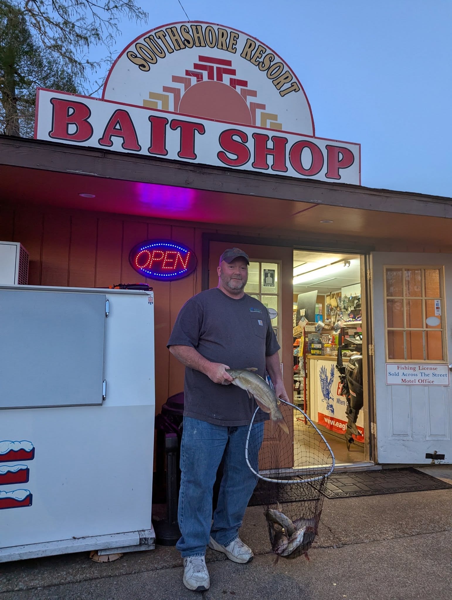 Man holding a net full of catfish in front of the Southshore Resort Bait Shop at dusk