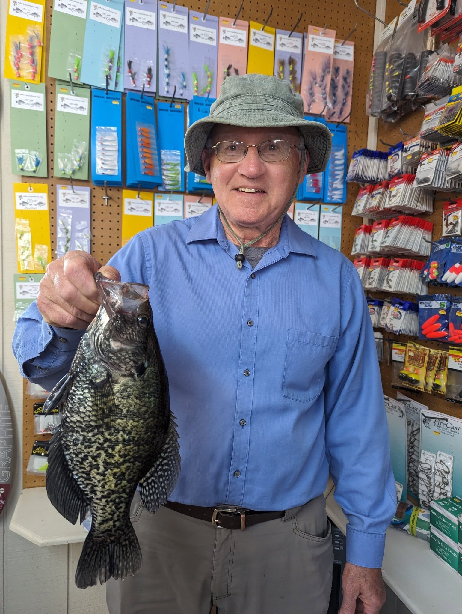 Man in blue shirt holding a large crappie in front of the tackle display wall