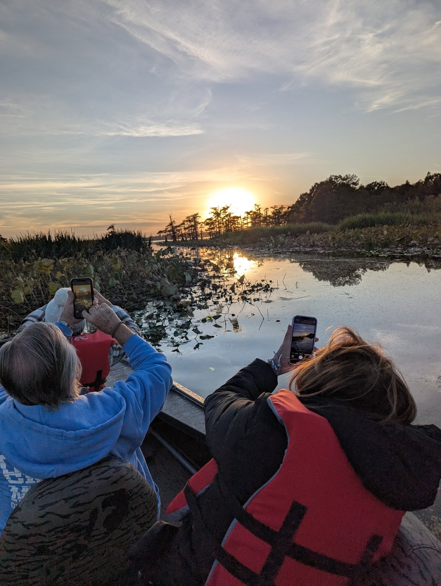 Two guests photographing the sunset over the cypress wetlands from the boat