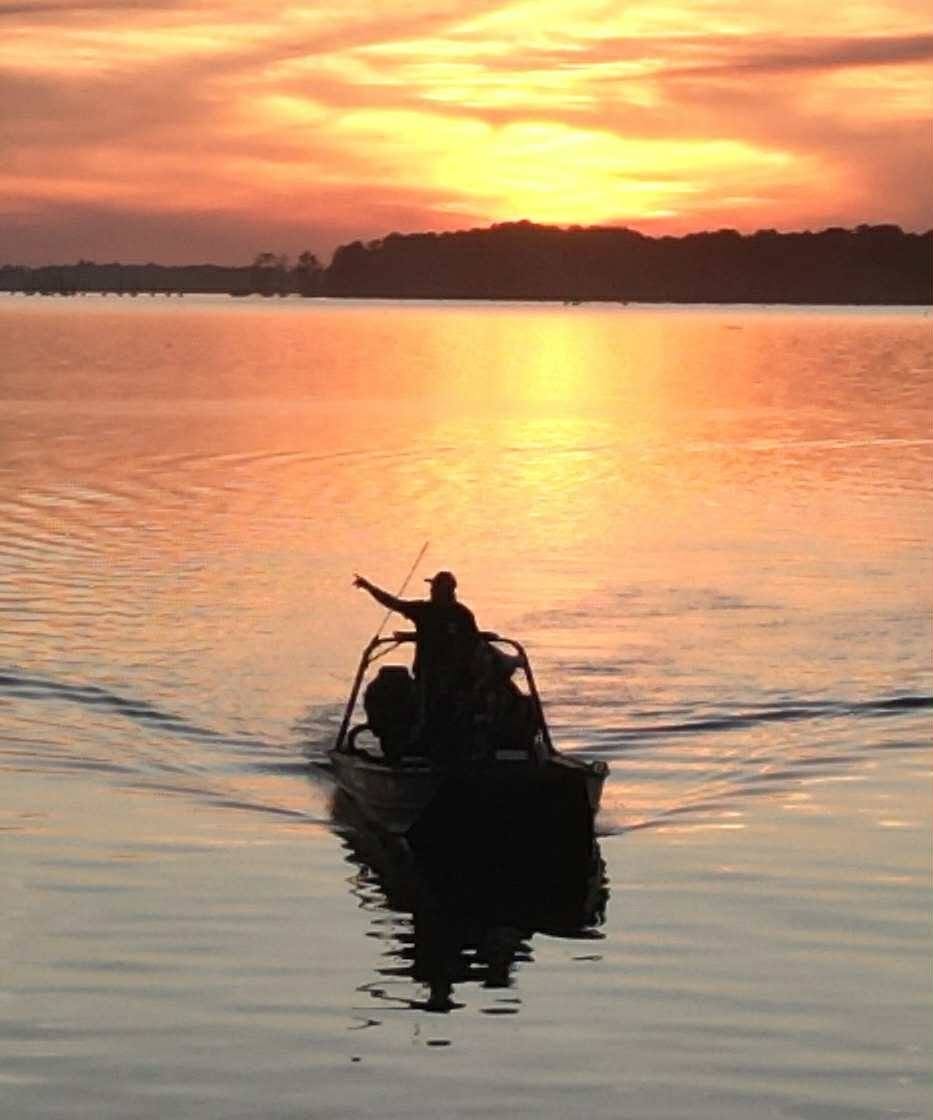 Silhouette of a guide pointing from a boat on Reelfoot Lake at sunset