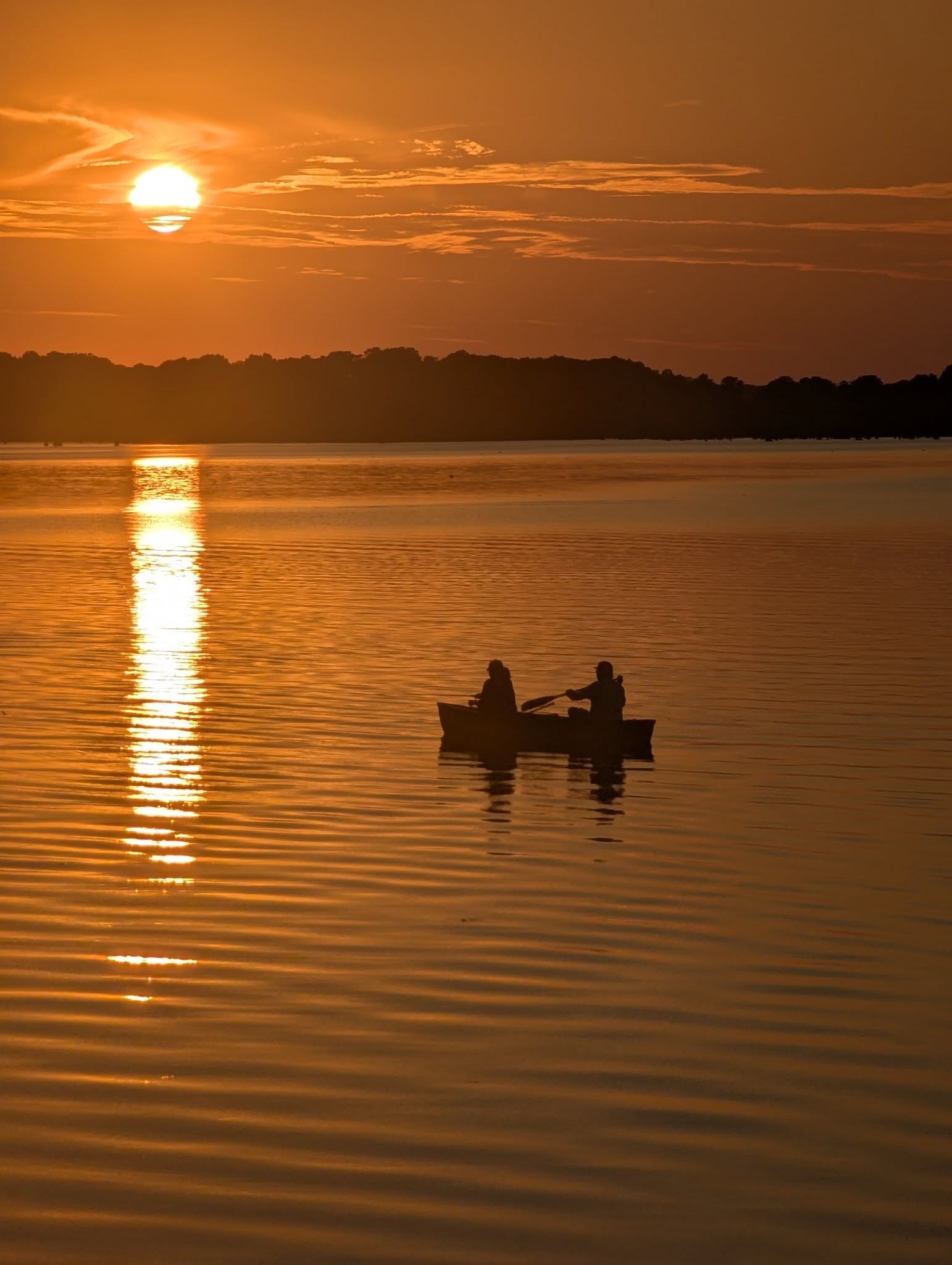 Two people paddling a canoe on Reelfoot Lake at golden-hour sunset