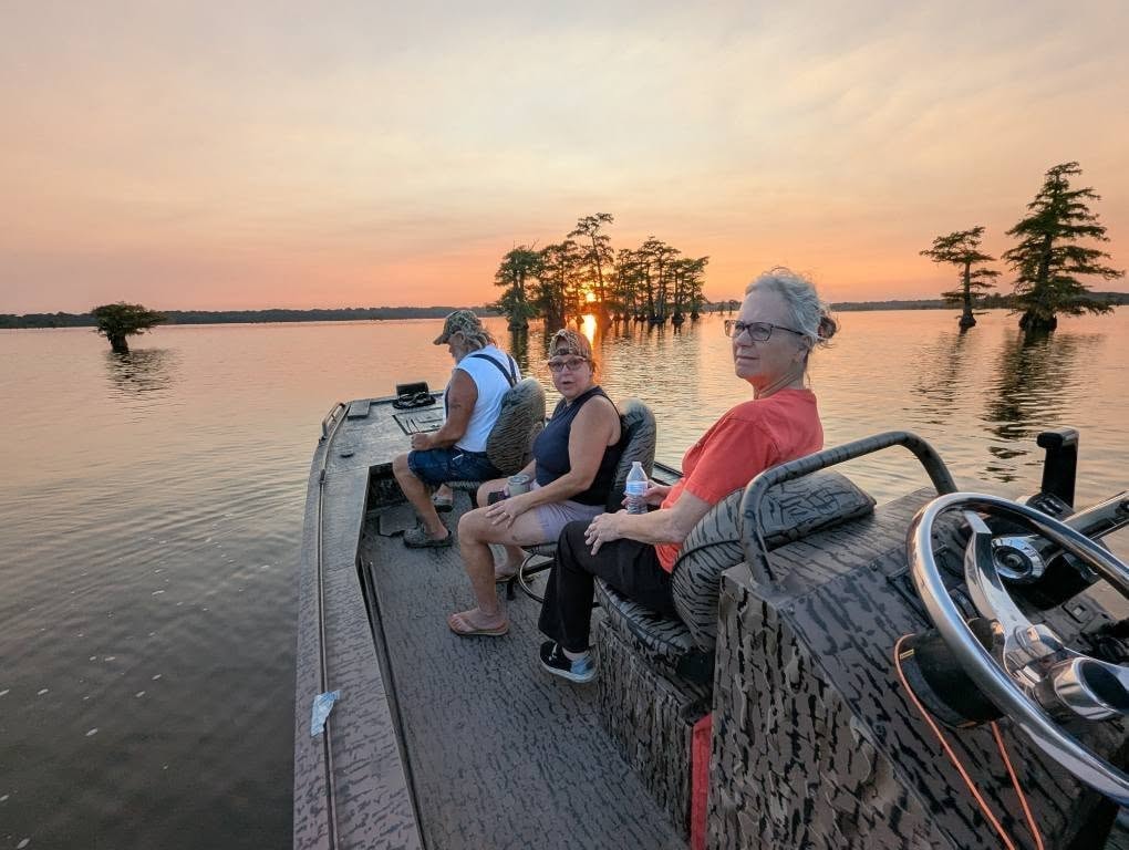 Three guests relaxing on a boat tour watching the sunset over Reelfoot Lake cypress trees