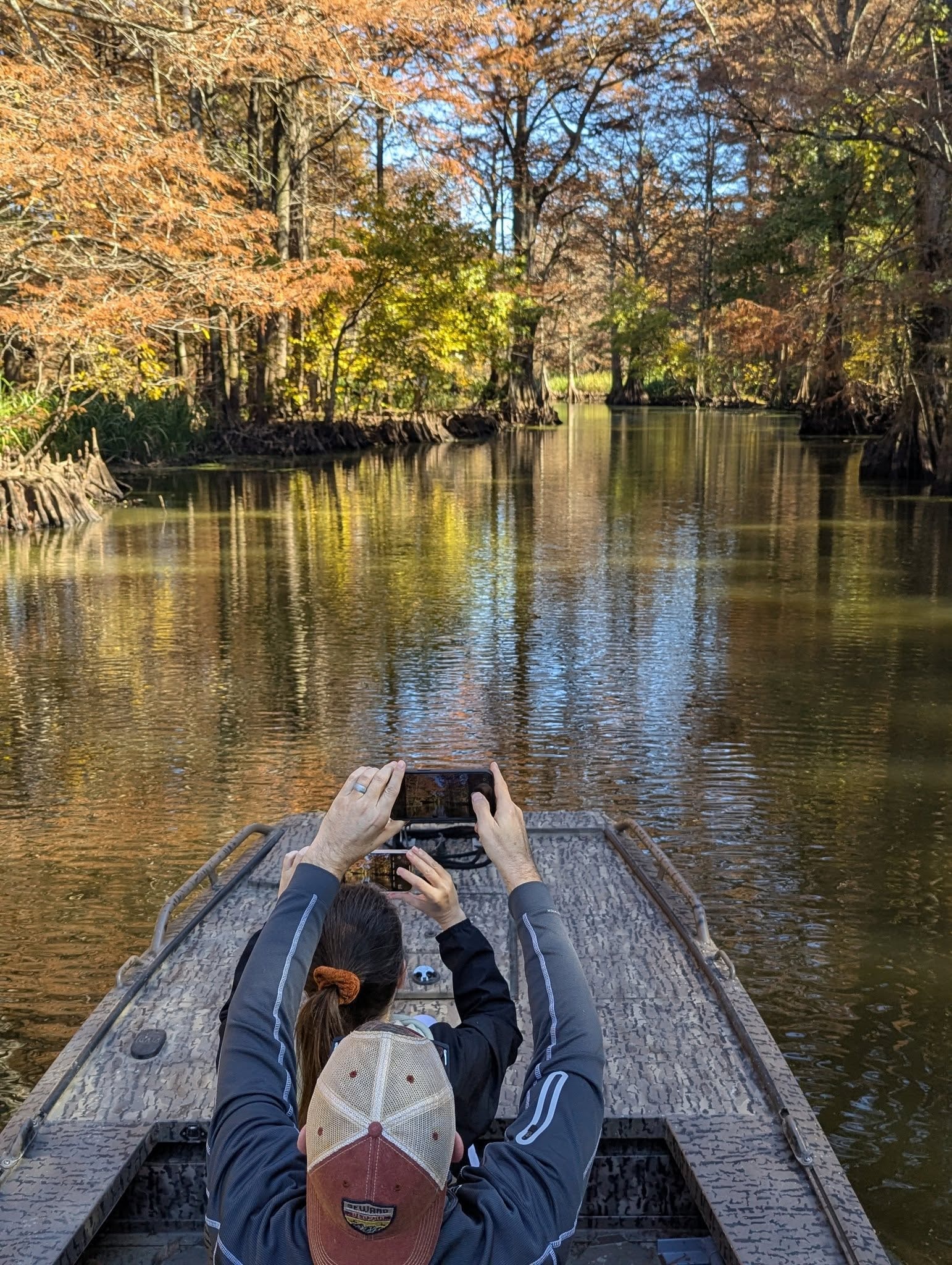Guest photographing the scenic cypress-lined waterway from the bow of the boat
