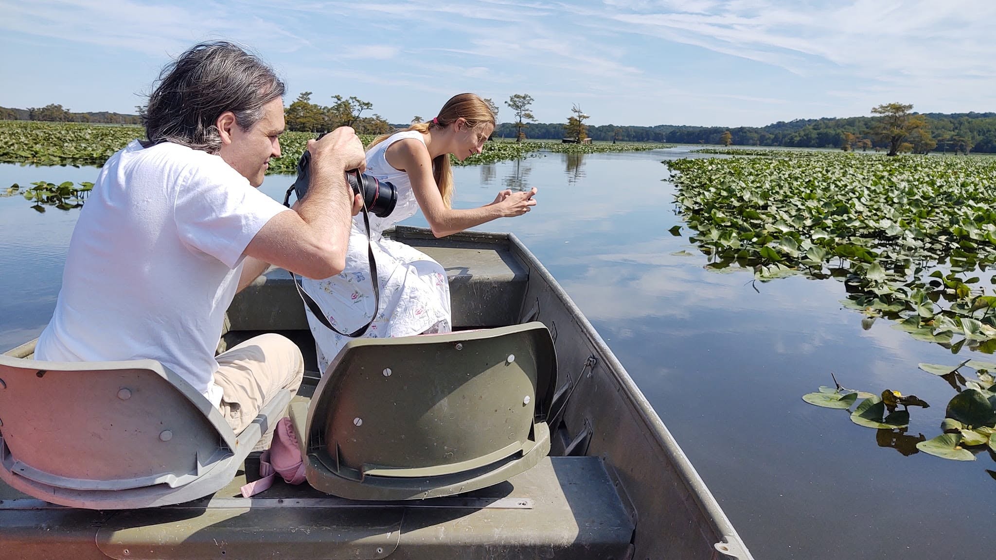 Couple photographing lotus pads from the bow of a jon boat on Reelfoot Lake