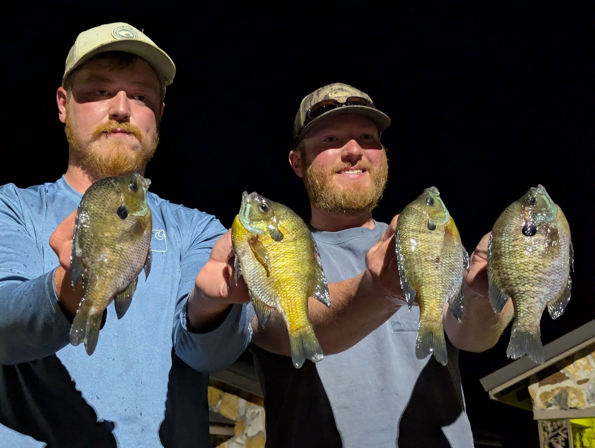 Two brothers holding bluegill catches at night
