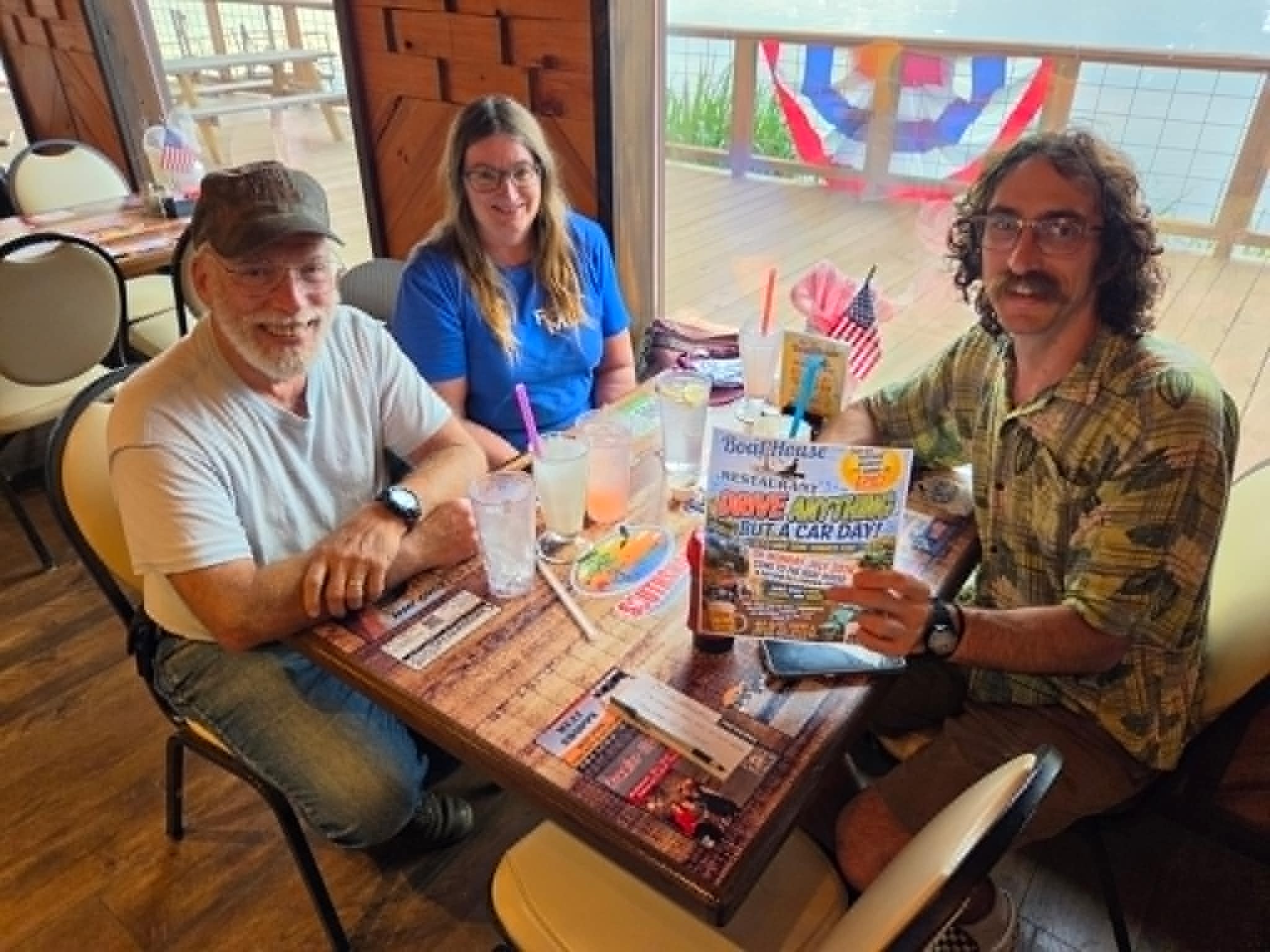 Three guests dining at The Boat House Restaurant holding a Cruise-In event flyer