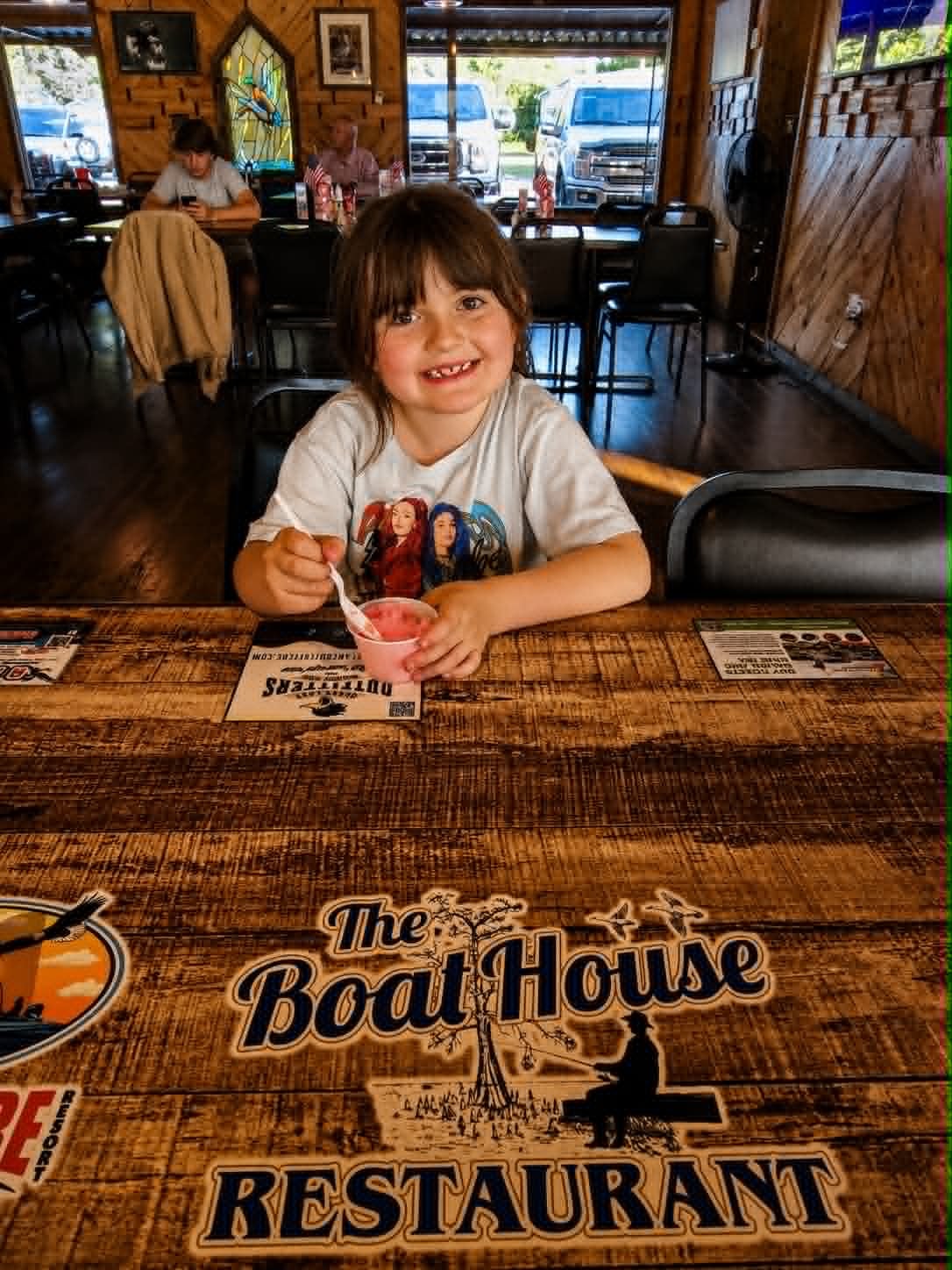 Young girl smiling at The Boat House Restaurant table with the restaurant logo visible