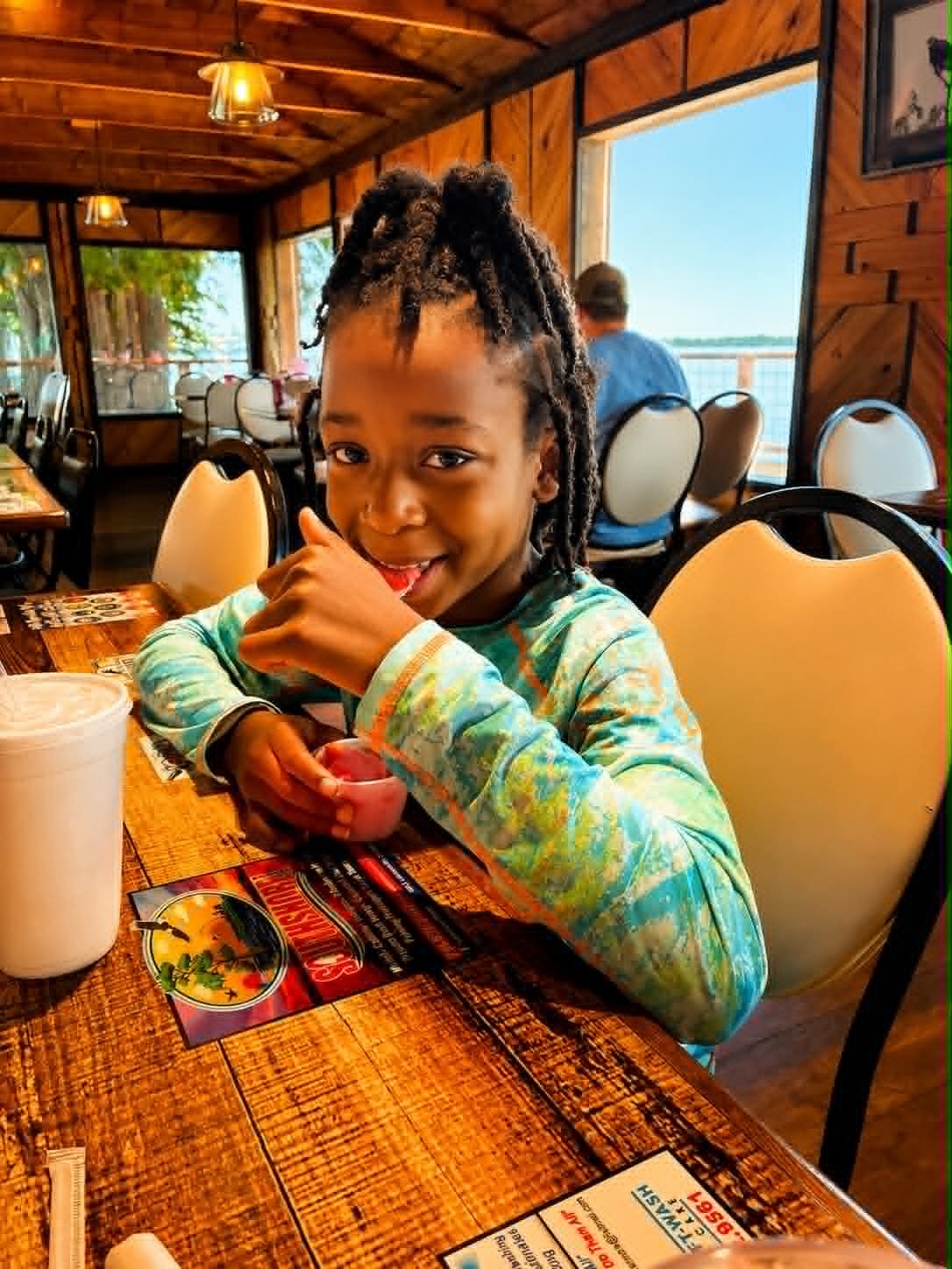 Young girl smiling at The Boat House Restaurant table with lake views through the windows