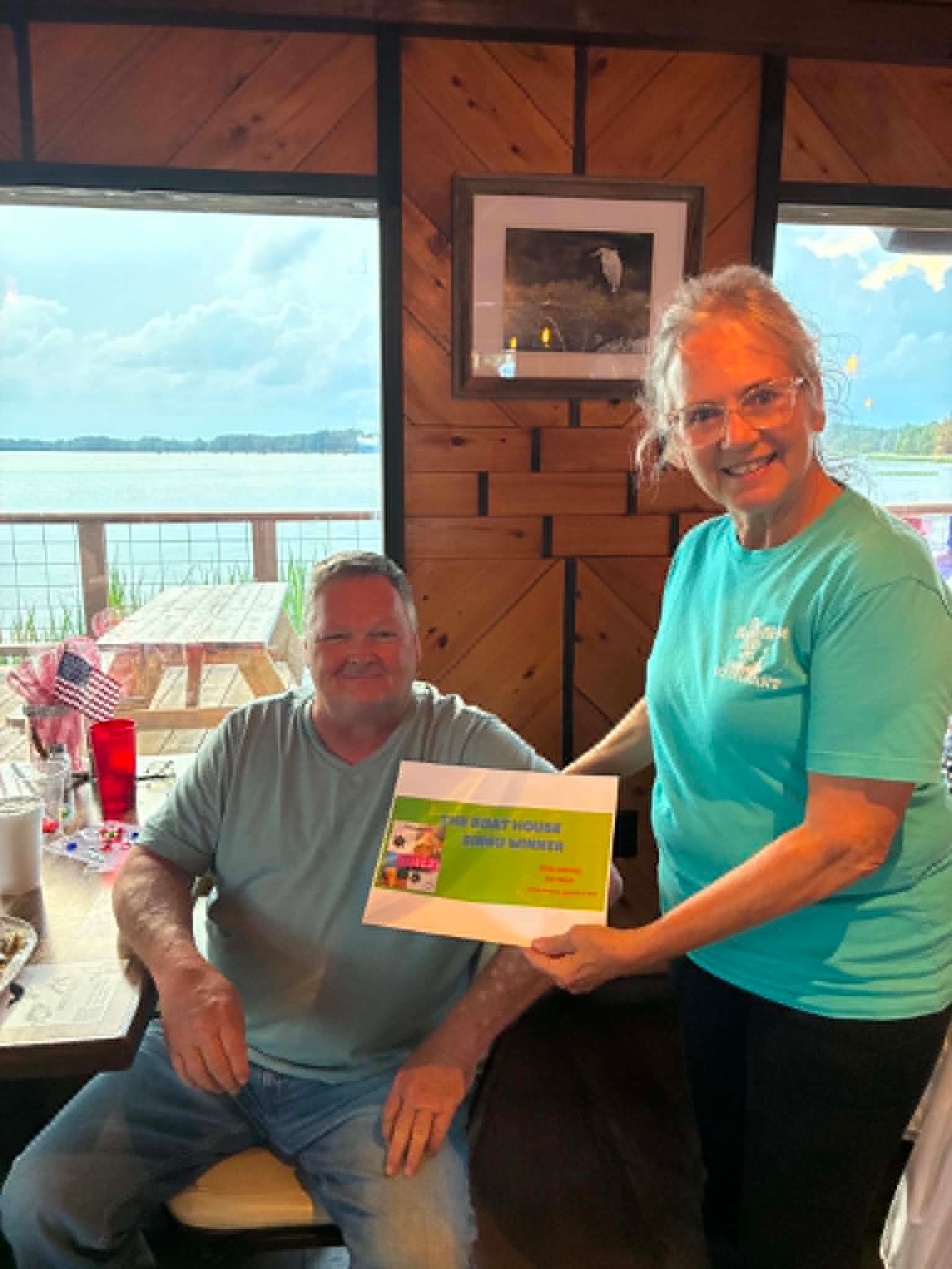 Boat House Bingo winner receiving certificate with lake views at The Boat House Restaurant