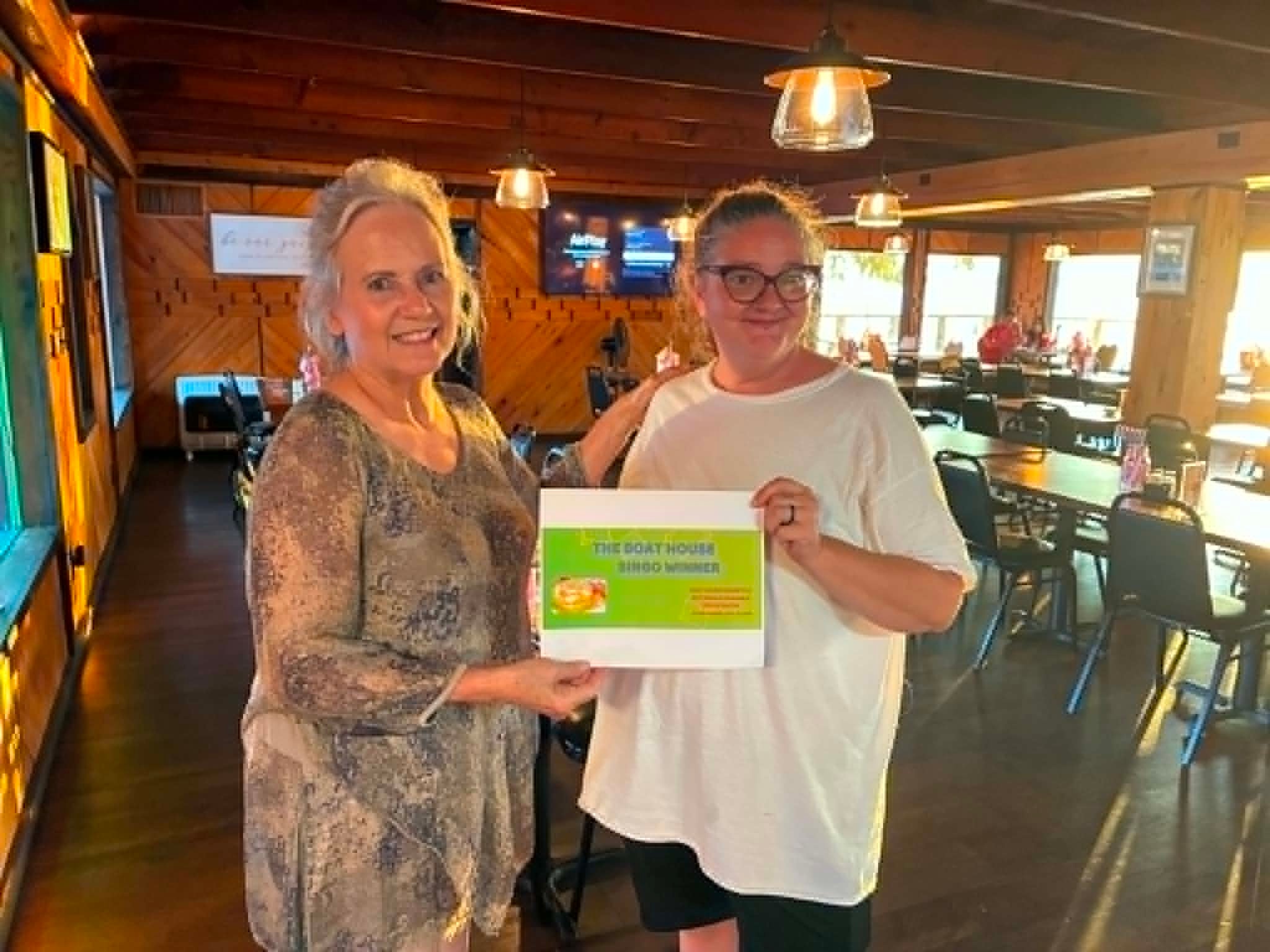 Two women holding Boat House Bingo winner certificate inside the restaurant