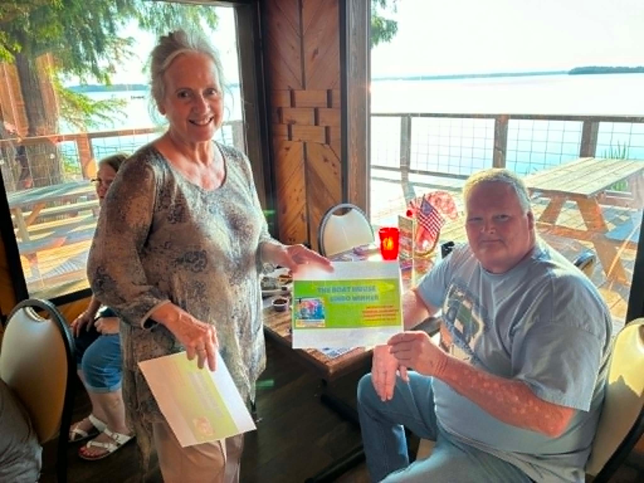 Boat House Bingo winner with certificate by the lakeside windows