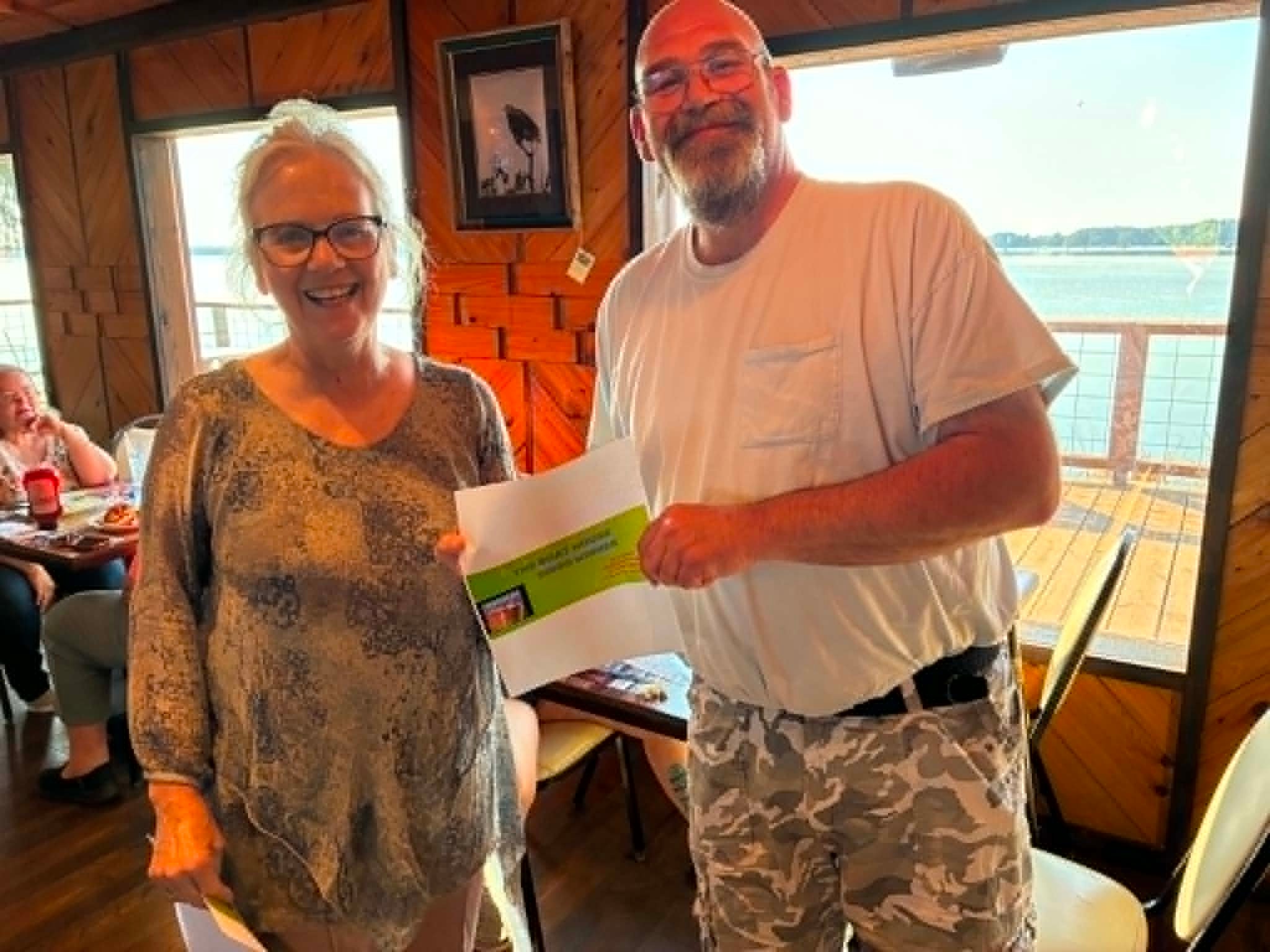 Boat House Bingo winner holding certificate with lake views at The Boat House Restaurant