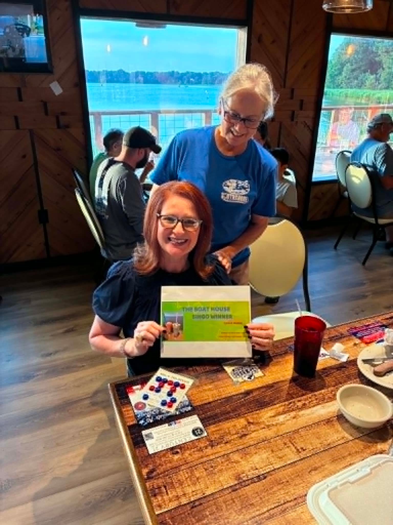 Boat House Bingo winner with certificate at lakeside table
