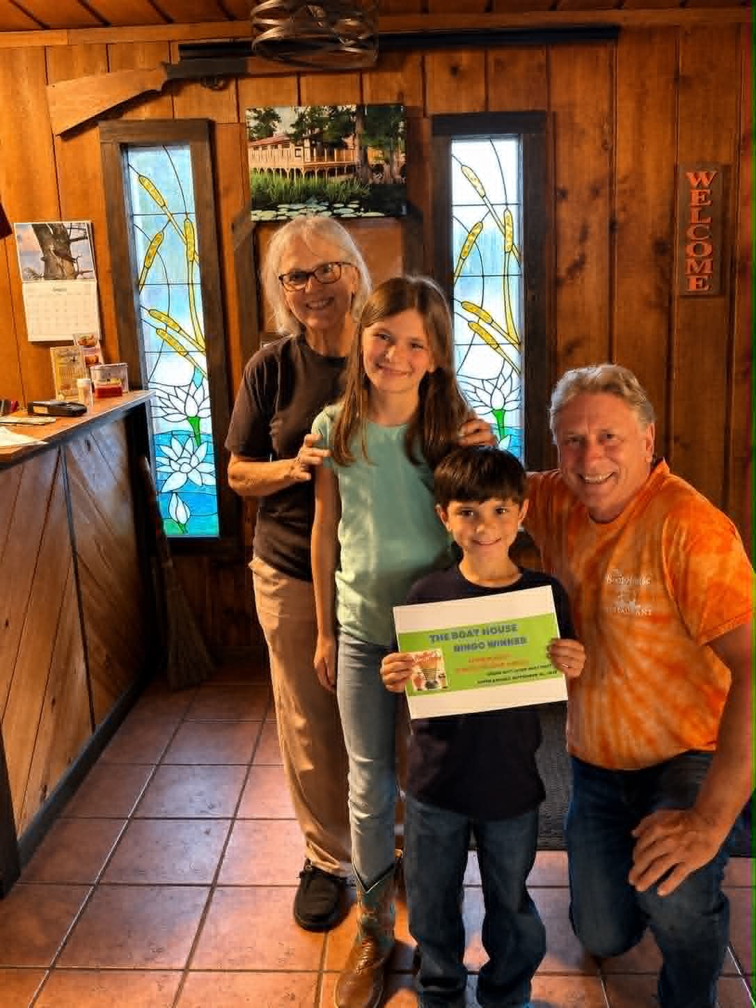 Family of four holding a Boat House Bingo winner certificate in front of the stained glass entry doors